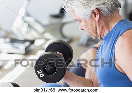 Stock Photo - Older Hispanic man lifting weights in gym. Fotosearch