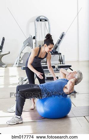 Picture - Older Hispanic man working with trainer in gym. Fotosearch
