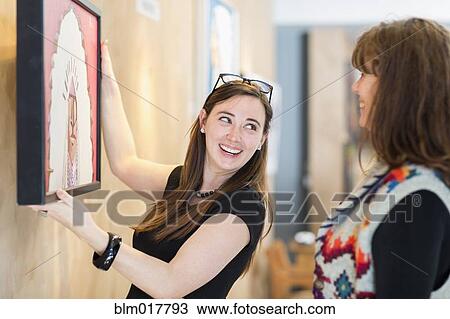 Stock Image - Women hanging painting on wall. Fotosearch