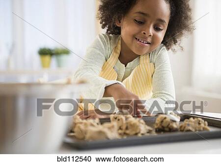 Stock Image - African American girl baking cookies in kitchen. Fotosearch