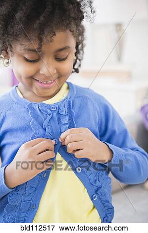 Stock Photo - African American girl buttoning her cardigan. Fotosearch