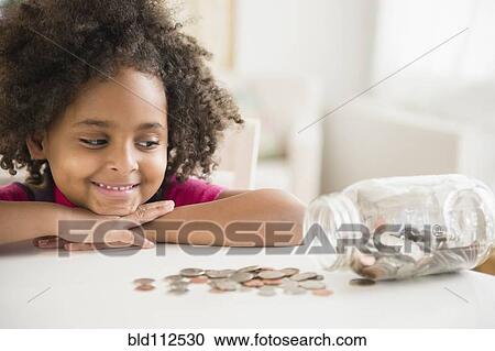 Stock Image - African American girl counting change in jar. Fotosearch