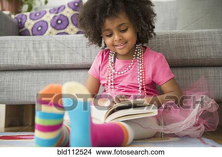 Picture - African American girl reading in living room. Fotosearch