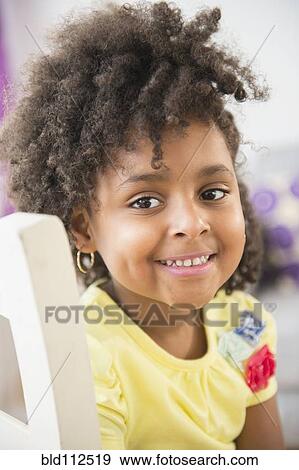 Stock Photo - African American girl smiling in chair. Fotosearch