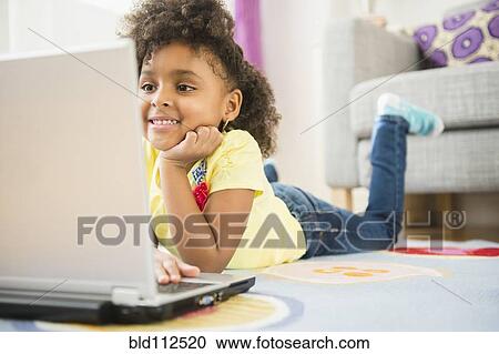 Stock Image - African American girl using laptop on floor. Fotosearch