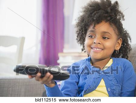Stock Photography - African American girl watching television on sofa. Fotosearch