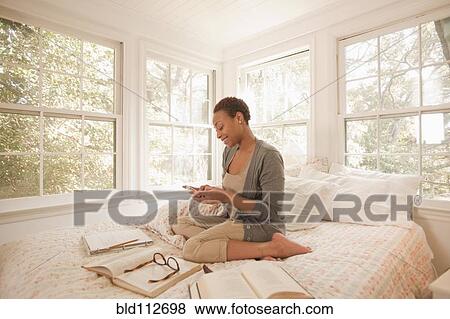 Stock Photo - African American woman studying in bed and using cell phone. Fotosearch