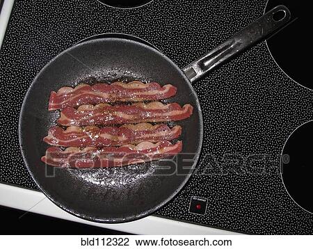 Stock Image - Bacon frying in pan on stove top. Fotosearch