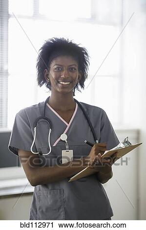 Stock Image - Black nurse writing on clipboard. Fotosearch