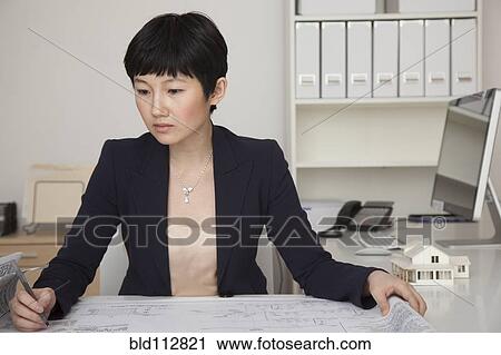 Stock Image - Businesswoman examining blueprints in office. Fotosearch