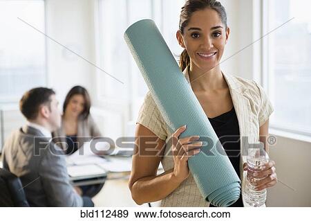 Stock Photo - Businesswoman holding yoga mat in office. Fotosearch