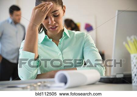 Stock Photography - Businesswoman rubbing her forehead at desk. Fotosearch