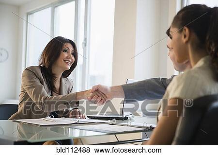 Stock Photo -  Businesswoman shaking hands with clients at desk. Fotosearch