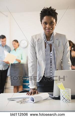 Stock Photograph - Businesswoman standing at desk in office. Fotosearch