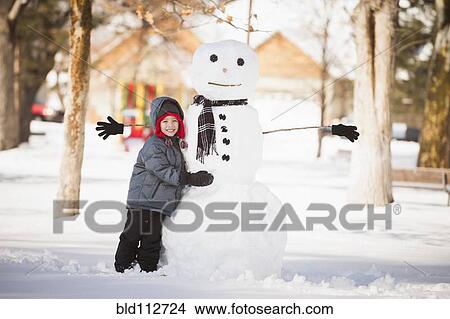 Picture - Caucasian boy building snowman in snow. Fotosearch