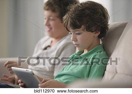 Stock Image - Caucasian boy using digital tablet on sofa. Fotosearch