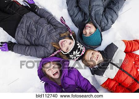 Stock Image - Caucasian children laying in snow outdoors. Fotosearch