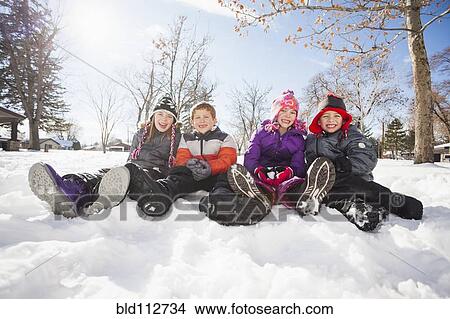 Picture - Caucasian children sitting in snow outdoors. Fotosearch