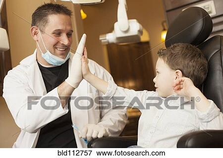 Stock Photo - Caucasian dentist and boy high fiving in office. Fotosearch