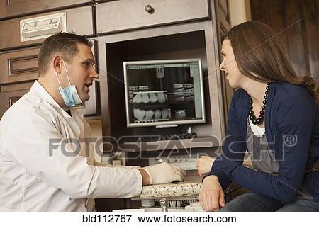 Stock Photo - Caucasian dentist and woman talking in office. Fotosearch