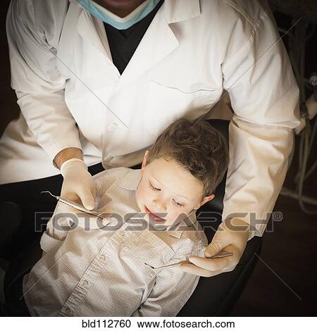 Stock Image - Caucasian dentist examining boy's teeth in office. Fotosearch