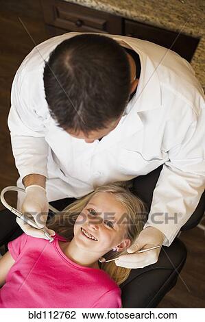 Stock Image - Caucasian dentist examining girl's teeth in office. Fotosearch