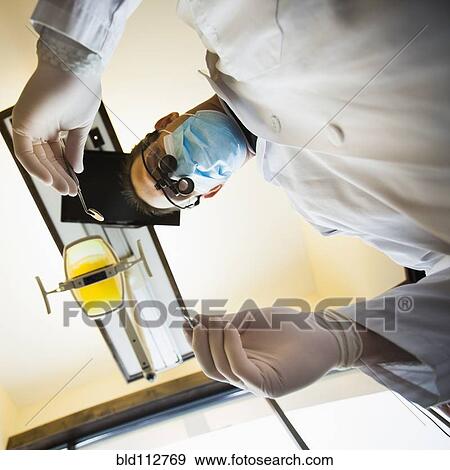 Caucasian dentist towering over patient in office View Large Photo Image Stock Photo - Caucasian dentist towering over patient in office. Fotosearch