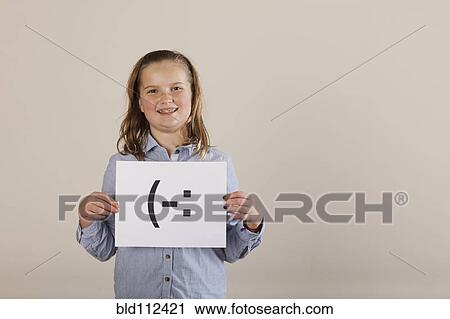 Stock Image - Caucasian girl holding card with smiley face. Fotosearch