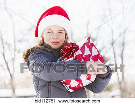Stock Image - Caucasian girl in Santa hat holding Christmas present. Fotosearch
