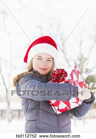 Stock Image - Caucasian girl in Santa hat holding Christmas present. Fotosearch