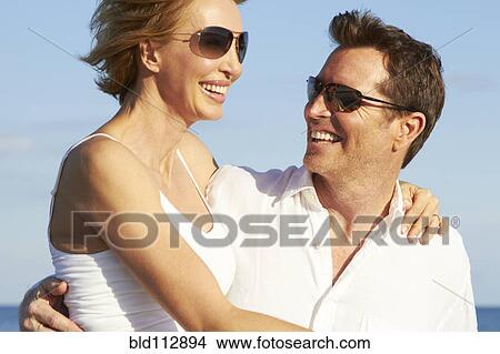 Picture - Caucasian man carrying girlfriend on beach. Fotosearch