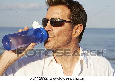 Caucasian man drinking water bottle on beach View Large Photo Image Stock Image - Caucasian man drinking water bottle on beach. Fotosearch