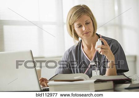 Stock Photo - Caucasian nurse looking at medicine bottle. Fotosearch
