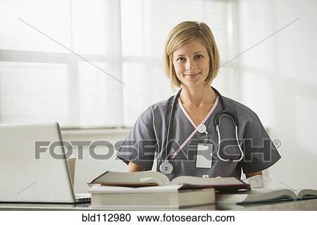 Stock Image - Caucasian nurse sitting with books and laptop. Fotosearch