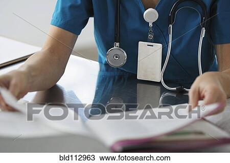 Stock Image - Caucasian surgeon reading book. Fotosearch