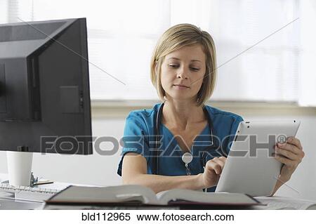 Stock Photography - Caucasian surgeon reading books and using digital tablet. Fotosearch