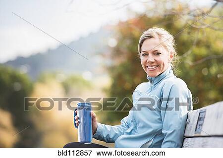 Stock Photo - Caucasian woman having coffee on park bench. Fotosearch
