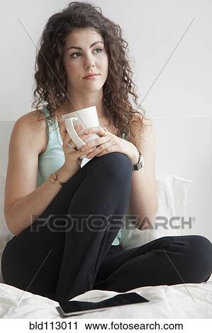 Caucasian woman sitting on bed drinking coffee View Large Photo Image Stock Image - Caucasian woman sitting on bed drinking coffee. Fotosearch