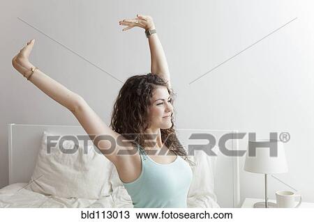 Stock Image - Caucasian woman stretching in bed. Fotosearch
