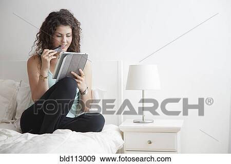 Stock Photo - Caucasian woman using digital tablet in bed. Fotosearch