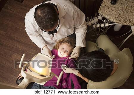 Stock Image - Dentist and nurse examining girl's teeth in office. Fotosearch