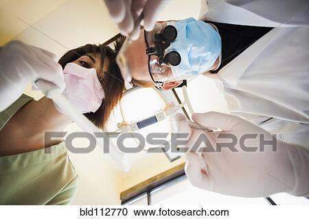 Dentist and nurse towering over patient in office View Large Photo Image Stock Image - Dentist and nurse towering over patient in office. Fotosearch