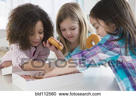 Stock Image - Girls eating donuts together in kitchen. Fotosearch