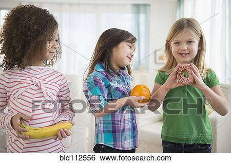 Stock Photograph - Girls eating fruit and donut in living room. Fotosearch