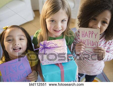 Stock Image - Girls holding presents and cards at birthday party. Fotosearch