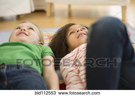 Stock Image - Girls laying on carpet in living room. Fotosearch