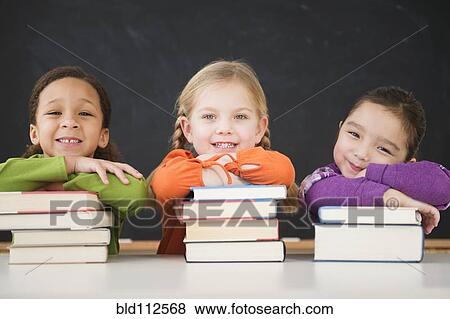 Stock Photo - Girls leaning on stacks of books in classroom. Fotosearch