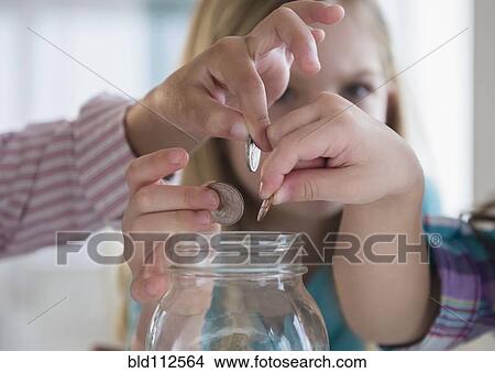Picture - Girls putting coins in savings jar. Fotosearch