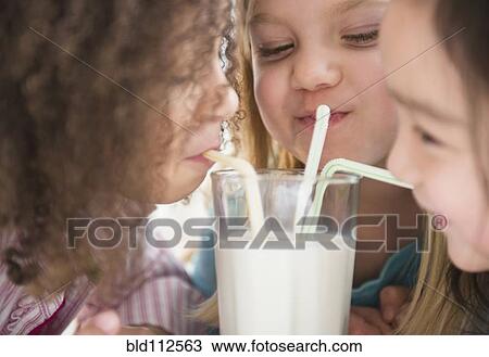 Stock Image - Girls sharing glass of milk. Fotosearch