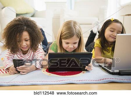 Stock Photo - Girls using technology on carpet. Fotosearch